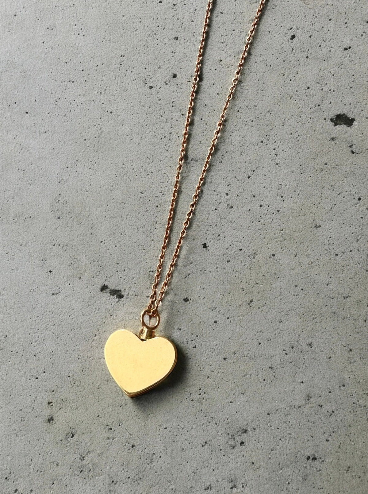 Gold heart-shaped pendant necklace to hold ashes on a gray concrete surface