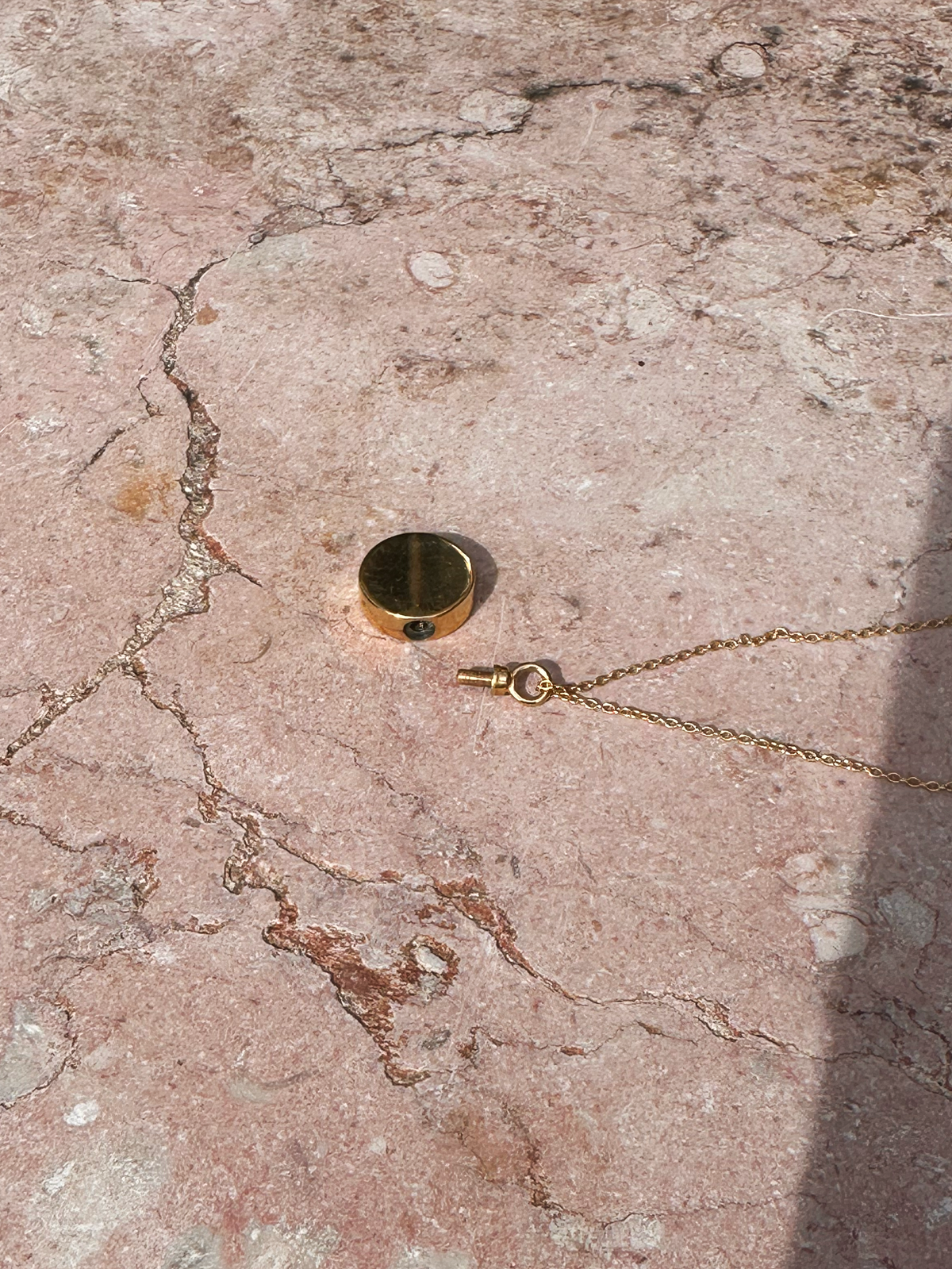 Gold memorial necklace with a round pendant to hold ashes on a textured stone surface, open to show how to hollow interior to hold ashes 