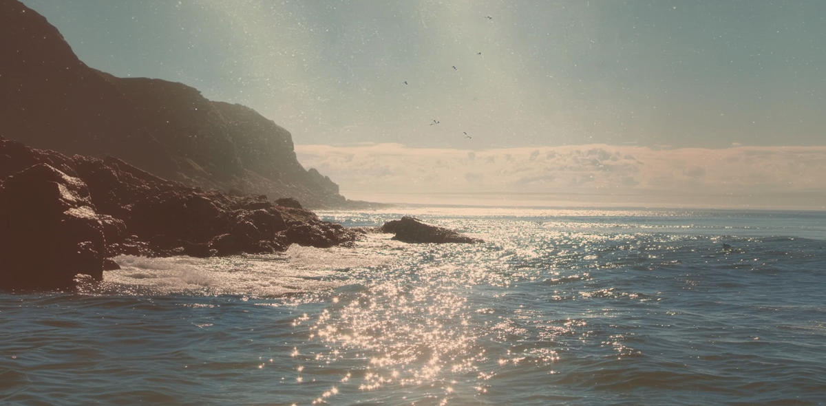 Rocks jutting out of the water with sunlight reflecting off the surface, creating a serene coastal scene.