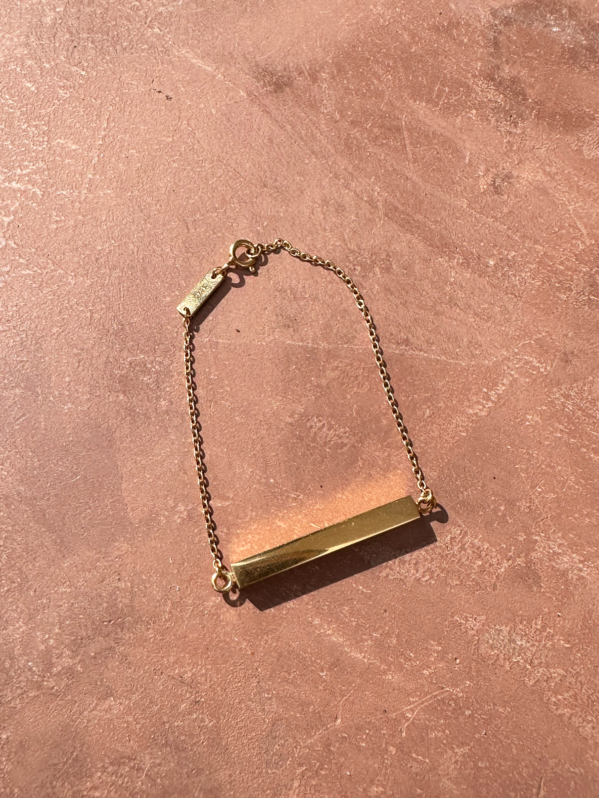 Gold memorial bracelet to hold ashes on a pinkish-brown surface