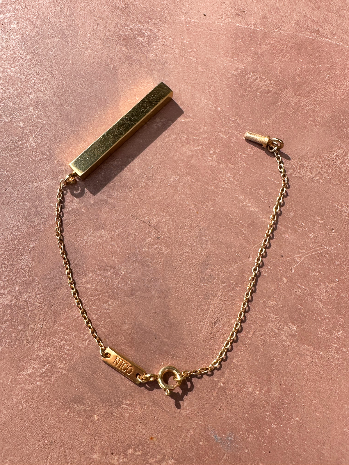 Gold memorial bracelet with screw enclosure to reveal hollow interior to hold ashes on a pink surface