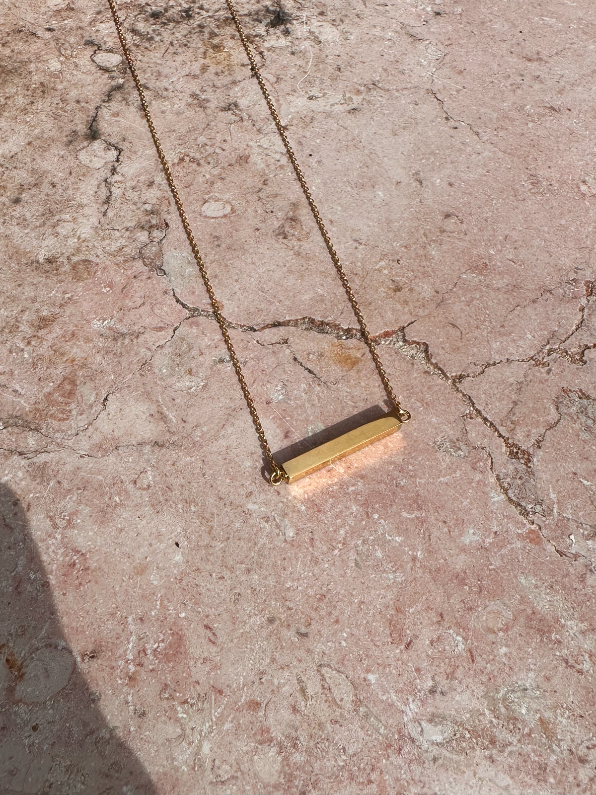 Gold necklace with a bar pendant to hold cremation ashes on a textured stone surface