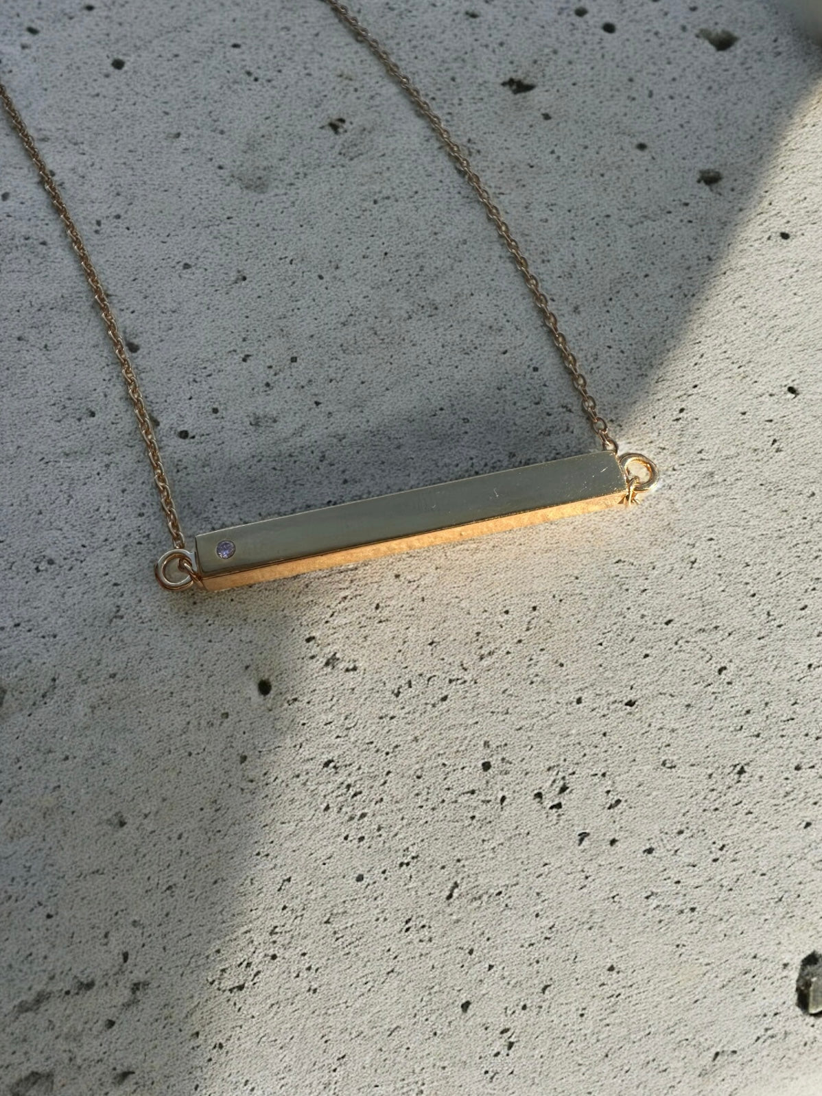 Gold  bar pendant necklace with gemstone on a concrete surface - necklace has a hollow interior to hold remembrance ashes